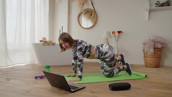 Lovely Sporty Fit Woman Watching Tutorial Video on Laptop Doing Donkey Kick Yoga Exercise at Home