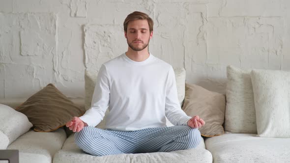 Wellness Young Man Sits on a Sofa in the Living Room and Meditates a Calm Mood Relaxing in a White