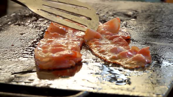 Closeup View of Thin Strips of Bacon Flipped of the Flat Grill Surface