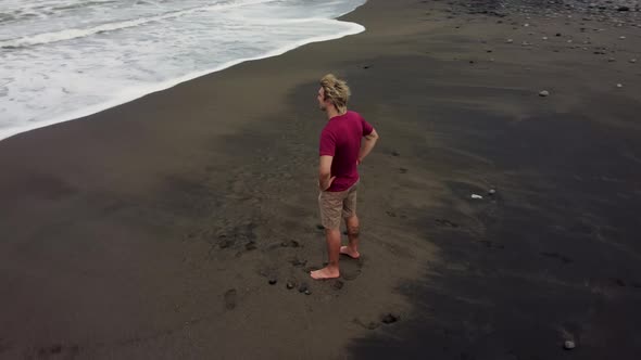 Man Looking in Ocean on Black Sand Beach