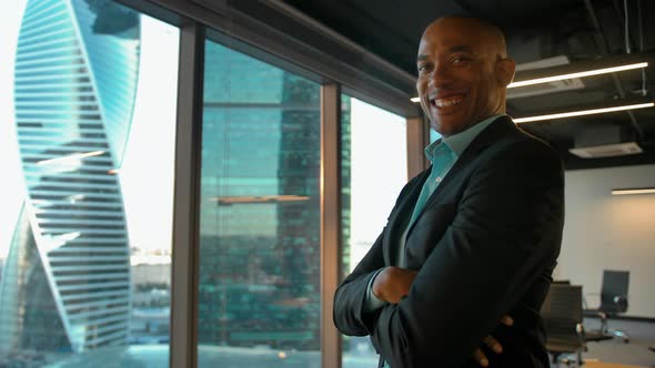 African American Boss Standing Near Huge Modern Office Window and Smiles.