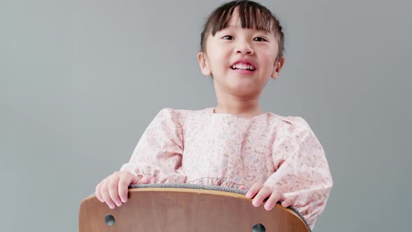 Cute little Asian girl in dress playing peek a boo on a chair, smiling, laughing and teasing with ha