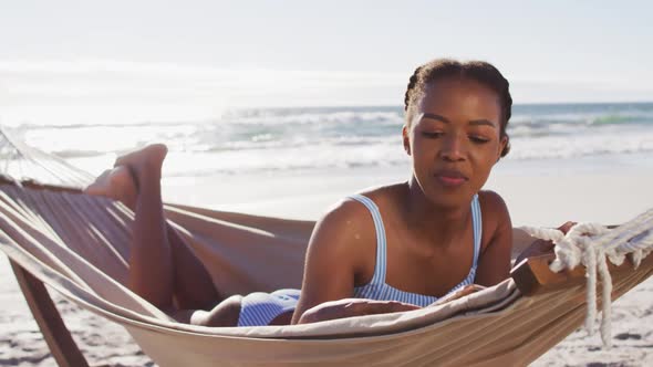 African american woman using digital tablet while lying on a hammock at the beach