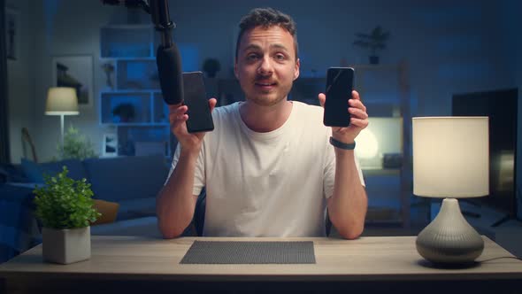 Young Handsome Man Makes an Overview of Two Smartphones at Home in the Living Room