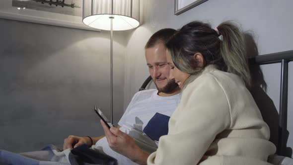 Caucasian husband and wife in pyjamas sitting up silently in bed at night, leaning on headboard