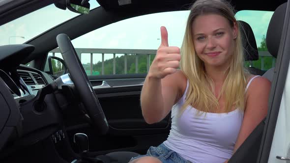 A Young Woman Sits Relaxed in a Luxurious Car and Shows a Thumb Up To the Camera with a Smile