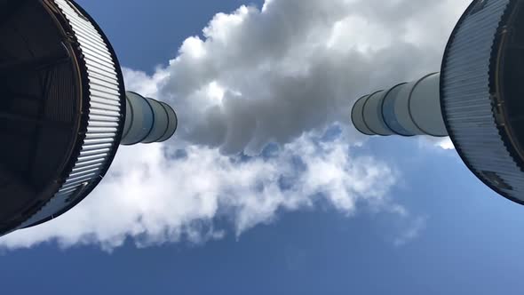 Smoking chimneys seen from below. White smoke against a blue sky