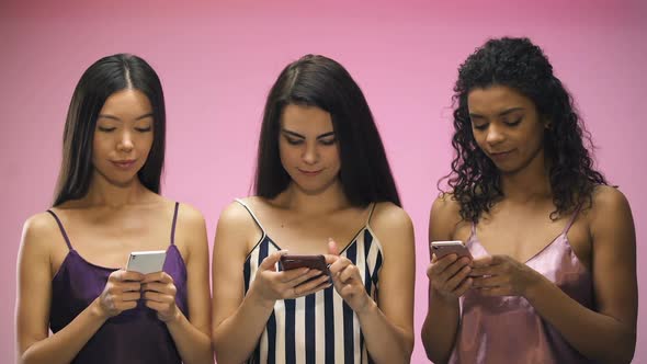 Female Friends in Pajamas Chatting on Smartphones, Isolated on Pink Background