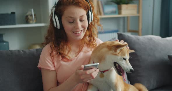 Beautiful Woman in Headphones Listening To Music and Petting Dog on Couch