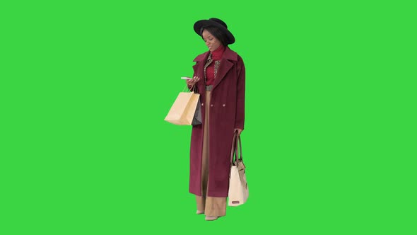 Smiling African American Fashion Girl in Coat and Black Hat Texting on Her Phone on a Green Screen