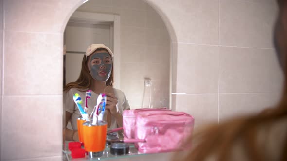 A Young Woman with a Mask on Her Face Dancing and Singing in Front of the Mirror