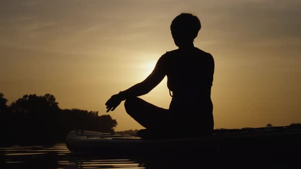 Silhouette of Woman Practicing Yoga on SUP Board at Sunset