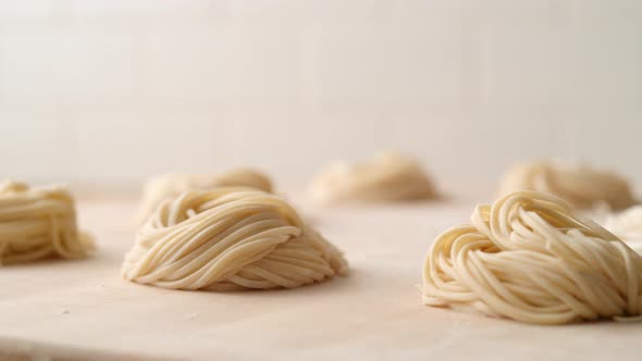 Camera follows piles of fresh pasta on wooden table. Slow Motion.