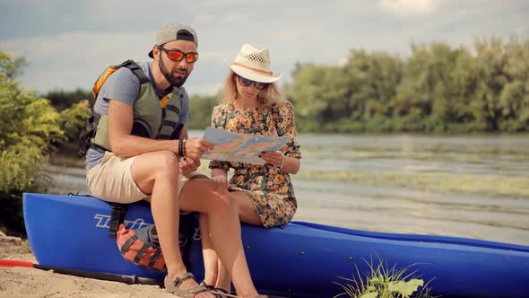 Two Tourist Traveler Sitting On Kayak At Weekend.Couple Searching Way On Map Holiday Vacation Trip.