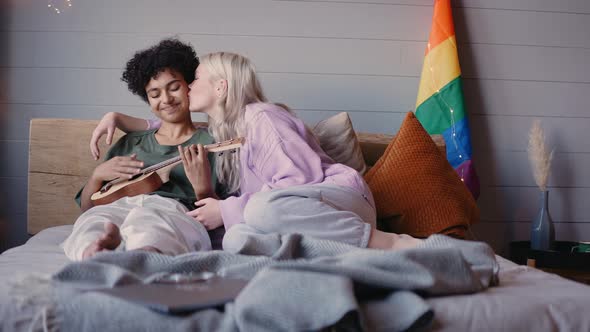 Young Girls Kiss Sitting on a Couch and Playing the Ukulele