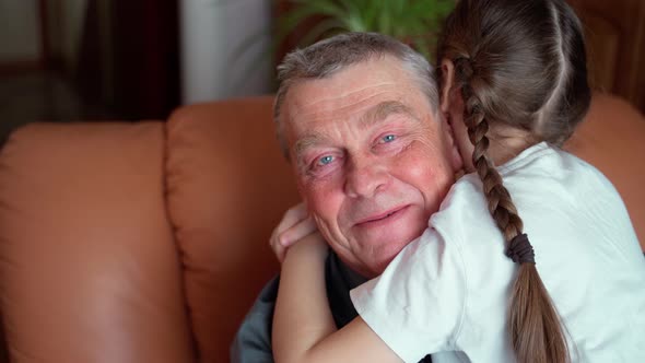 An elderly grandfather hugs his young unrecognizable granddaughter. Unrecognaziable girl