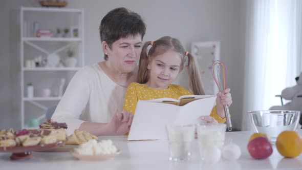 Portrait of Pretty Little Girl Sitting on Grandmother's Knees and Listening To Recipe. Young