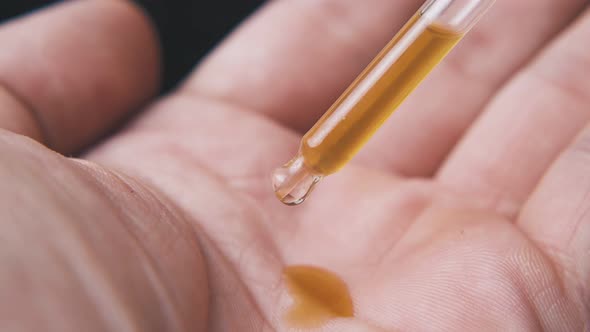 Person Drops Liquid From Pipette on Palm in Black Background