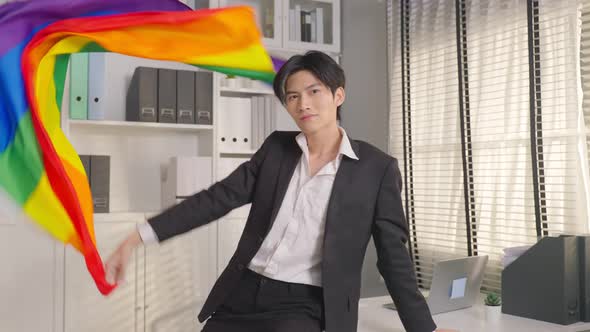 Portrait of Asian businessman gay working in office throwing LGBT flag then looking at camera.