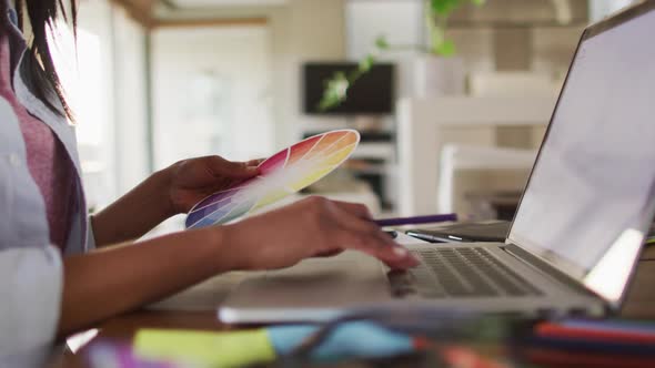 Mixed race woman using laptop writing in notebook drinking coffee working from home