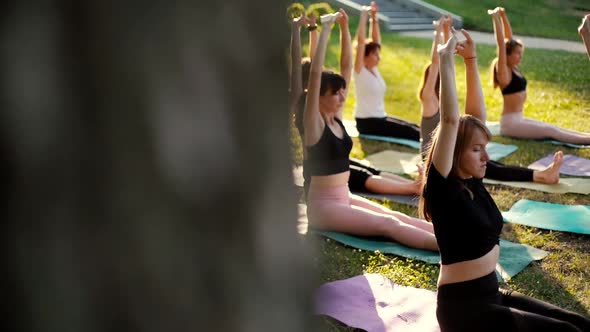 Group of Women Is Practicing Yoga and Sit with Hands Up Morning in Park