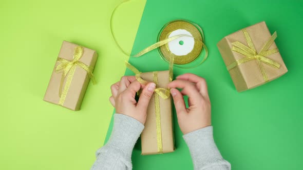 Woman packs gifts in brown paper and golden ribbon, green background