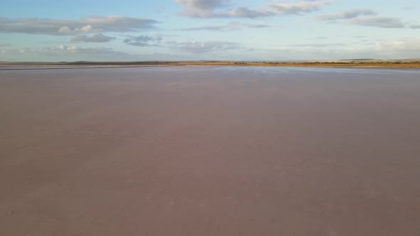 Drone aerial going sideways over shiny dry pink lake in Australia with a flat landscape