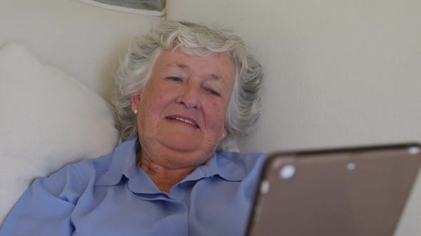 Caucasian senior woman using digital tablet while lying on the couch at home