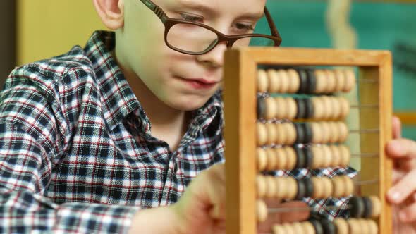 Portrait of a Caucasian schoolboy 7-8 years old wearing glasses counting on wooden abacus