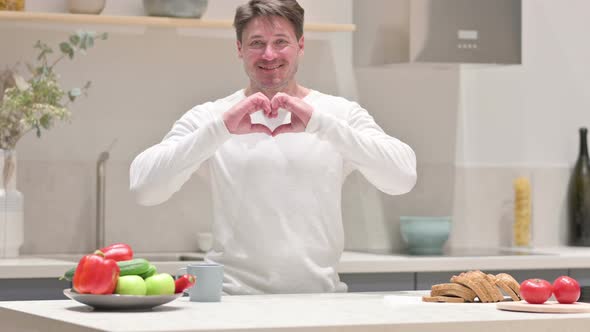 Middle Aged Man Making Heart Shape By Hands While in Kitchen