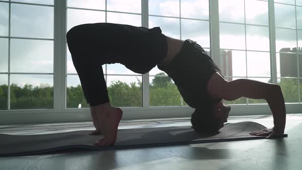 Wellness Young Man Doing Yoga in a White Room Filled with Light Man Performs the Bridge Pose Near