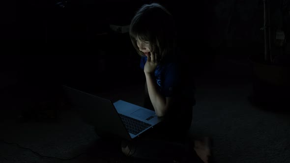 Close Up Shot of Little Boy Sitting on the Floor with a Laptop on the Internet at Night