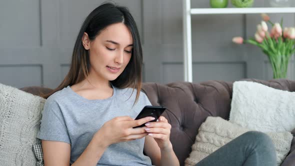 Young Pretty Woman Sitting on Sofa with Smartphone