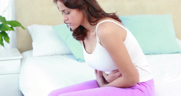 Woman sitting on bed with stomach pain