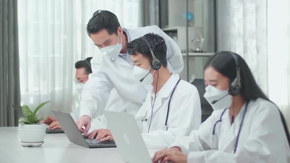 A Man Coming To Help One Man Of Three Asian Doctors In Masks Working As Call Centre Agent