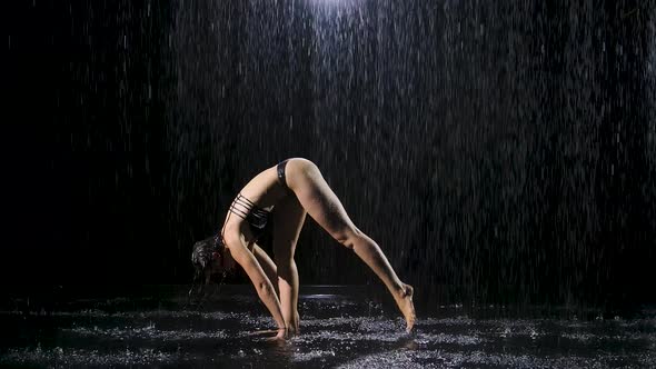 A Young Woman Doing Stretching Exercises Under the Streams of Rain. Drops of Water Fall on Body