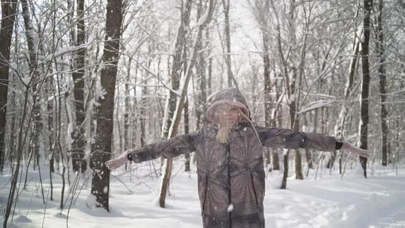 A young woman throws a handful of snow up making a snowfall.