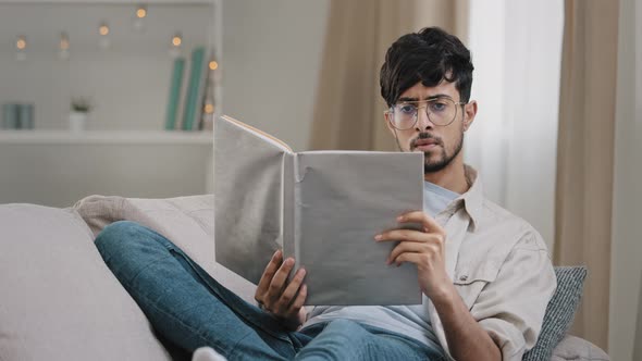 Arabic Young Smart Guy Student Bearded Man in Glasses Lies on Sofa at Home Reading Book Textbook