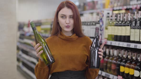 Attractive Redhead Caucasian Woman Choosing Between Red and White Wine in Alcohol Supermarket