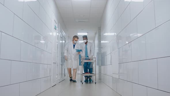 Doctor Talks with Nurse While Walking at the Hospital Hall Carrying Test Tubes