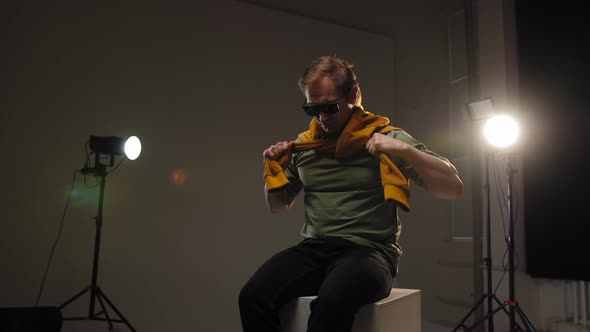 A Man with a Yellow Scarf Sits in the Middle of a Photo Studio