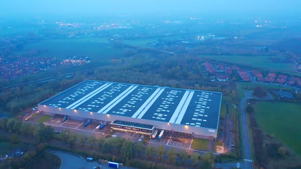 Aerial shot orbital around a warehouse at night (dusk), circled by vegetation. Wattrelos, France