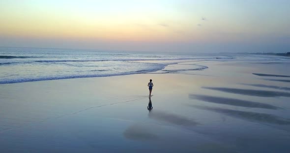 Aerial drone view of a young woman walking on the beach at sunset.