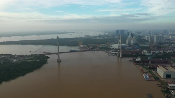 drone view flying away from large river suspension bridge and over industrial urban area of the city