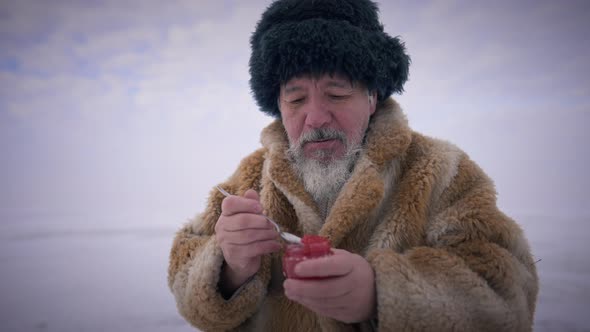 Old Man Eating Red Caviar with Spoon in Slow Motion Sitting at Picturesque Northern Landscape