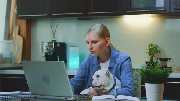 Young Woman Working on the Computer and Holding Small Dog on Her Hands