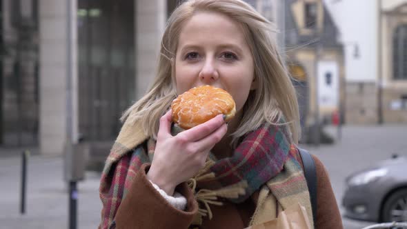 Young woman eating donut on the city street