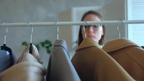 Young Woman in Glasses Chooses Clothes That Hanging on a Clothing Rack in a Shop