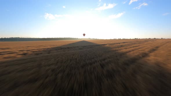 Orange Hot air ballon floating above sloping field at beautiful sunrise