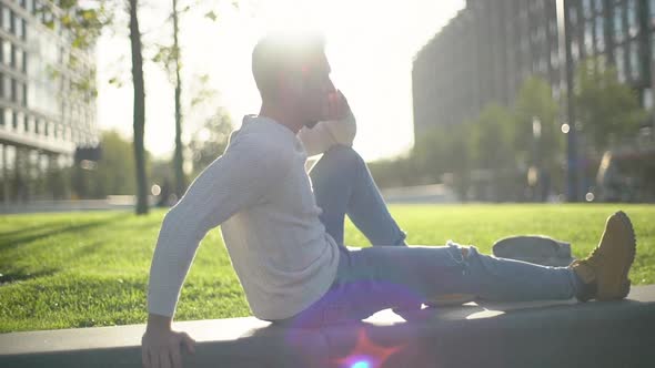 Slowmotion Attractive Blond Caucasian Male Adult Sitting Grass Relaxing Talking Mobile Phone